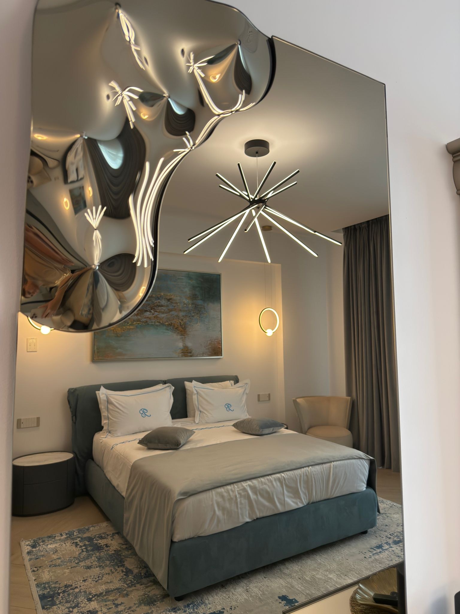 Oglindă decorativă care reflectă zona de dormit și lustra